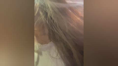 Media: A close-up video captures a person with long, wet, blonde hair, partially obscuring their face. The background is blurred, and the image appears to be taken in a bathroom, with a faint reflection of water droplets visible.