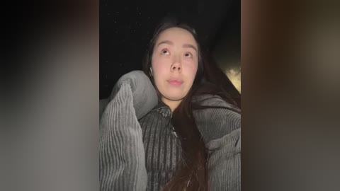 Media: A video of a young woman with long, dark hair, wearing a gray, ribbed sweater, lying on her back, with a dark, starry night sky visible in the background.