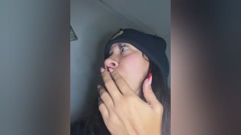 Media: Video of a young woman with light skin, wearing a black beanie and red-painted nails, holding a large, erect penis, looking shocked.