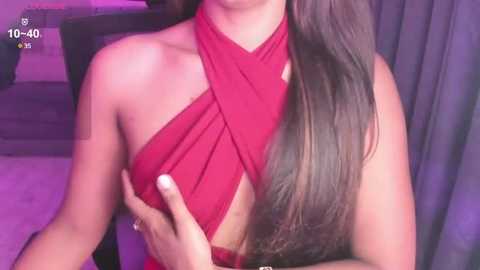 Media: Video of a woman with long, straight, dark brown hair, wearing a red halter dress, holding her breast. Background features purple lighting and a gray curtain.