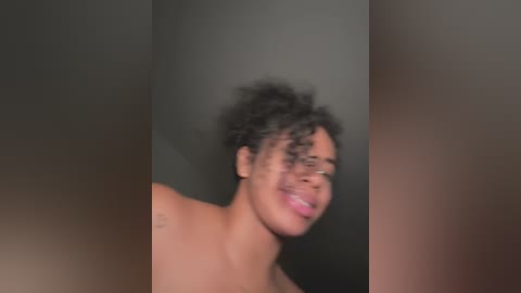 Media: A video of a smiling, light-skinned Black woman with curly hair and glasses, her topless torso partially visible, against a blurred background.