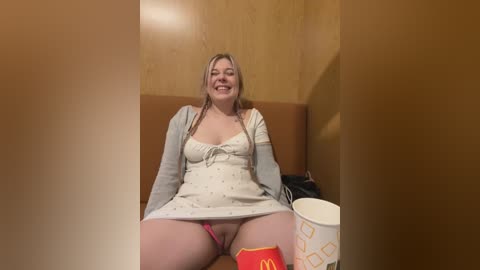 Media: A video of a smiling, plus-sized Caucasian woman in a McDonald's uniform, wearing a grey dress and red thigh-high socks, sitting on a brown bench against a wooden wall.