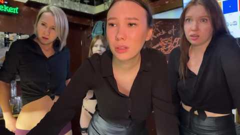 Media: Video of three young women, two in black shirts, one in a black dress, in a dimly lit bar; one holds a beer bottle.