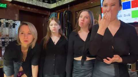 Media: Video of four women, two wearing black tops and high-waisted jeans, one in a black top and denim shorts, and one in a black top and skirt, posing in a dimly lit store.