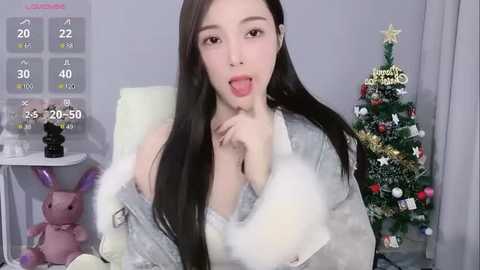 Media: A video of an Asian woman with long black hair, wearing a revealing, fluffy white outfit, posing seductively in front of a Christmas tree.