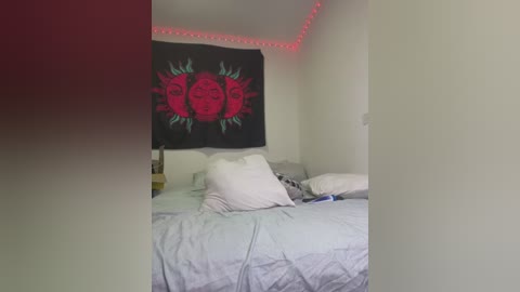 Media: Video of a messy bedroom with a black tapestry featuring a sun with red and green details hanging above a bed with white sheets and pillows. Red LED lights line the ceiling, giving a warm glow.