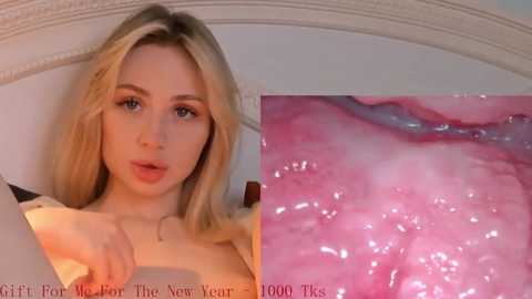 Media: A close-up photo of a young woman with fair skin and long blonde hair, lying on a white bed with a pinkish, moist, close-up of her vaginal opening in the background.