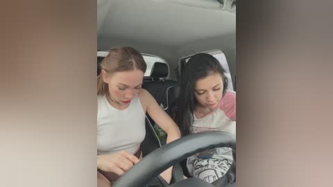 Video of two young women, one with light skin and blonde hair, another with darker skin and black hair, sitting in a car.