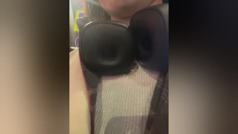 Media: A video of a person wearing large, black over-ear headphones, with a blurred background suggesting an indoor setting. The person's face is partially visible, and they are wearing a light-colored, possibly beige or cream-colored shirt.