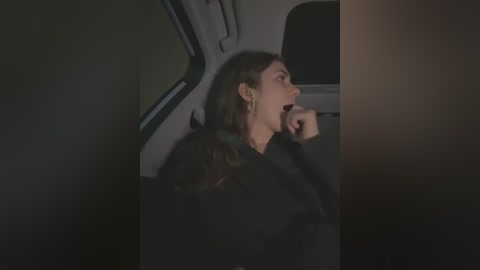 Media: A dimly lit video captures a woman with long brown hair and a black jacket, resting her head on her hand, seated in a dimly lit car interior.