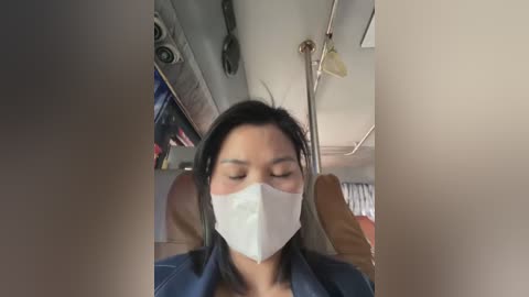 Media: A video of a woman wearing a white face mask, seated in a bus, with blurred backgrounds, showing a casual, everyday moment.