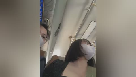 Media: A video of an Asian woman with a mask, short black hair, and a dark dress, taken in a dimly lit airplane bathroom.