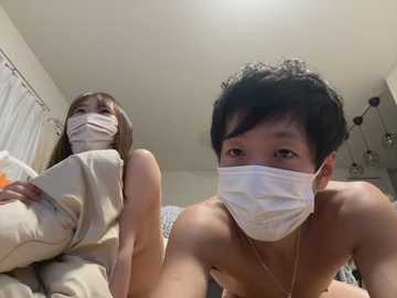 Media: Video of two Asian individuals in a bedroom, wearing white face masks, one with a short black haircut and the other with long brown hair. They are shirtless and appear to be in a casual, intimate setting.