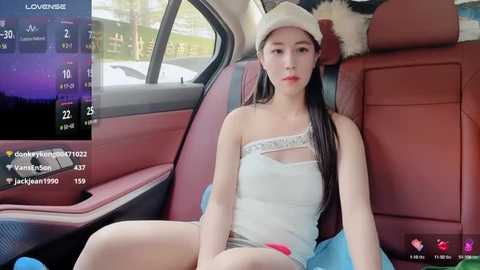 Media: Video of an Asian woman with long black hair, wearing a white hat and sheer top, sitting in a red car interior.