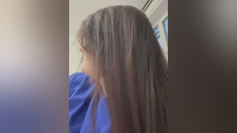 Media: Video of a child with long, straight, light brown hair, wearing a blue shirt, viewed from the side, partially obscured by a lens flare.