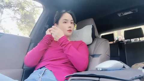 Media: Video of a woman with dark hair, wearing a pink sweater, resting in the backseat of a car. Inside the car, there are multiple computer screens and a mouse.