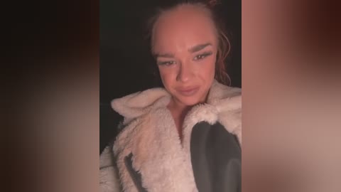 Media: A video of a young woman with light skin, wearing a fluffy white and black fur coat, standing against a dark background. She has dark hair and is looking down with a slight smile.