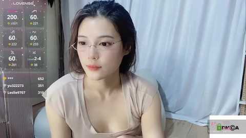 Media: A video of a young East Asian woman with straight black hair, fair skin, and glasses, wearing a light pink top. She sits in front of a white curtain background, with a live stream overlay displaying temperature and time.