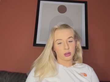 Media: Video of a blonde woman with light skin, wearing a white shirt, with closed eyes, leaning back, against a maroon wall with a framed abstract art piece.