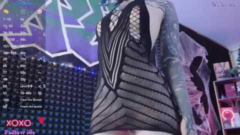 Media: Video of a woman in a black, fishnet dress with a sheer, leaf-like pattern, showing tattoos on her arms. Background shows a stadium with empty seats and a purple, star-shaped light. Text overlays include \"XOXO\" and \"Pewdiepie\" logos.