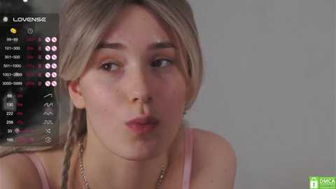 Media: Video of a young woman with light skin and straight blonde hair, wearing a pink top, puckering her lips. Background shows a live stream with a chat window.