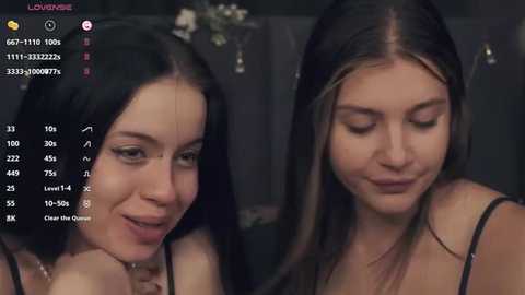 Media: Video of two young women, one with long black hair and the other with long brown hair, smiling and looking at each other, in a dimly lit room.