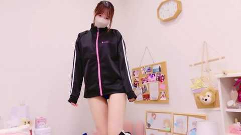 Media: Video of an East Asian woman in a black Adidas tracksuit, standing in a pastel-colored room with wall decorations, including a clock and stuffed toys.