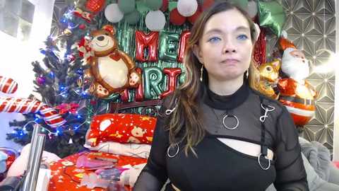 Media: Video of a woman with long brown hair, wearing a black mesh top with metal rings, standing in a festive, decorated room filled with holiday balloons, presents, and a Christmas tree.