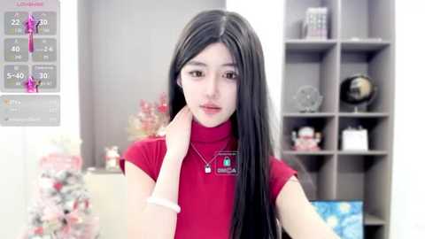 Media: Video of a young East Asian woman with long black hair, wearing a red turtleneck and a white smartwatch. She stands in a modern, brightly-lit room with gray shelves and decorative items in the background.