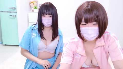 Media: Video of two Asian women in hospital gowns, one with a large chest, the other with a small chest, in a sterile room with a turquoise cabinet.