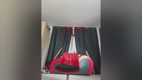 Media: Video of a cluttered, dimly lit room with a red and gray recliner chair, black curtains, and a wooden door.