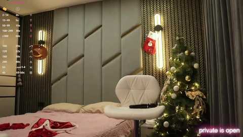 Video of a modern bedroom with a white upholstered chair, a cozy Christmas tree, and a neatly made bed adorned with festive red and gold decorations.