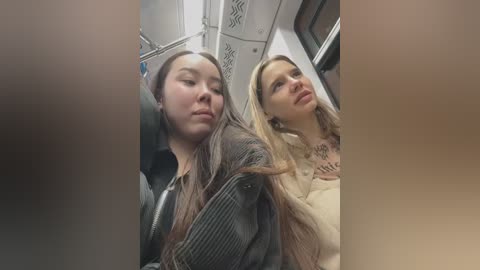 Media: Video of two young women seated on a train; one with long, straight hair in a grey jacket, the other with long, wavy blonde hair in a beige sweater.