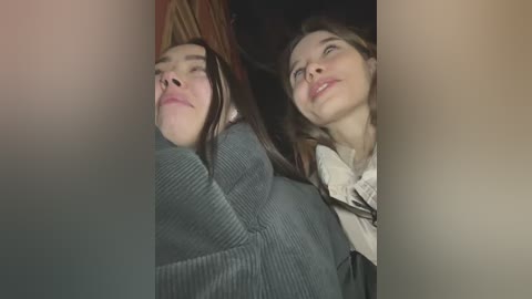 Media: Video of two young women, one with long hair, lying with eyes closed, the other with short hair, looking upward, both in dark clothing.