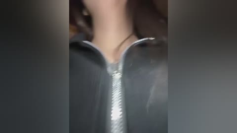 Media: A close-up video of a woman\u2019s neck and chest in a black leather jacket with a silver zipper. Her skin is light, and she wears a necklace. The background is blurred.