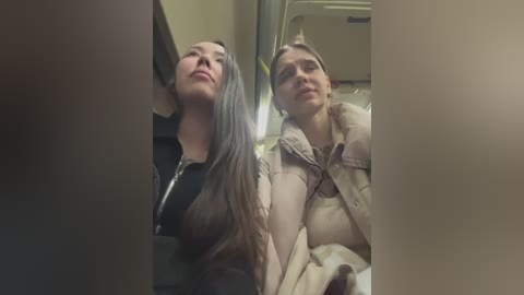 Media: Video of two women in an airplane, one Asian with long black hair, the other Caucasian with blonde hair, both wearing jackets, looking out windows.