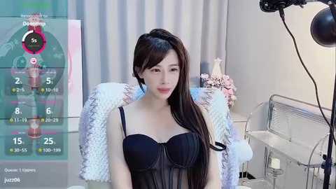 Media: Video of an Asian woman with long black hair, wearing a black lace bra, sitting in a chair in a modern room with a white fur throw and a monitor displaying a health app.