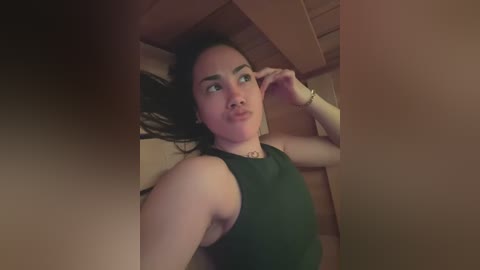 Media: A video of a young woman with long black hair, wearing a dark green sleeveless top, lying on a wooden floor, looking contemplative.