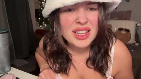 Media: Video of a young woman with fair skin, dark hair, wearing a Santa hat, a white lace bra, and a nose ring. She's smiling widely, indoors, with a cozy background featuring Christmas decor.