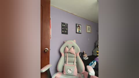 Video of a cozy, pastel-themed room with a light purple wall, featuring a plush Hello Kitty gaming chair, framed anime artwork, and a cluttered desk.