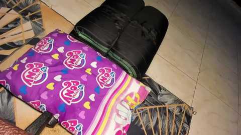 Media: Video of a woman sleeping on a tiled floor, using a black sleeping bag and a purple pillowcase adorned with \"Panda\" designs.