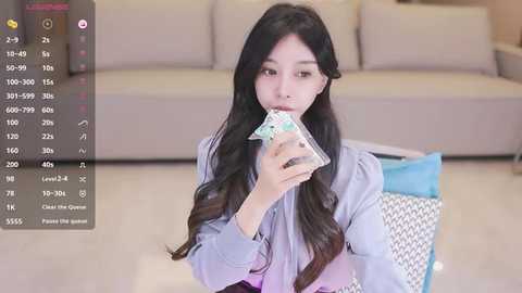 Media: Video of a young Asian woman with long black hair, wearing a light purple shirt, sitting on the floor, holding a plastic bag with money, in a modern living room with beige sofa.