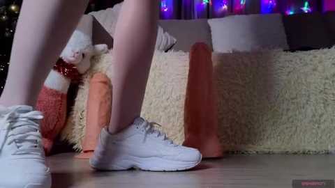 Media: A video shows a person in white socks and sneakers standing on a fluffy, cream rug, with a plush toy and colorful string lights in the background.