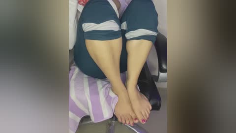 Media: A video of a woman's legs and feet, wearing dark green leggings and red-painted toenails, sitting on a chair with a purple and white striped towel draped over the seat.