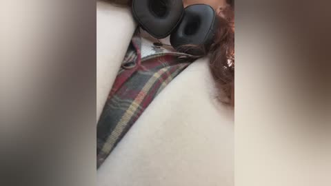 Media: Video of a close-up view of a person wearing a plaid-patterned thong underwear and black headphones, with a blurred background.