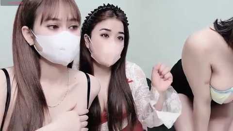 Media: Video of three young Asian women in a bathroom. One is wearing a face mask, another has long brown hair, and the third is topless.