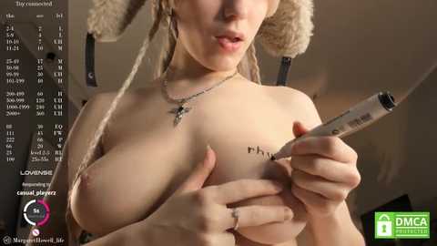 Media: Video of a topless woman with light skin, large breasts, and blonde dreadlocks, holding a pen over her tattooed chest. Background shows a calendar with dates, and a watermark reads \"DMCA Takedown Notice.\