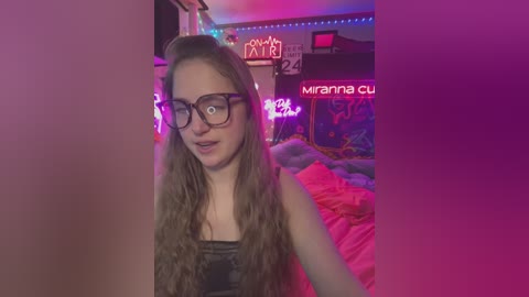 Media: Video of a young woman with long, wavy hair, wearing glasses, a black top, and pinkish-purple room with neon signs, including \"Mariana cut,\" and a bed with pink sheets.