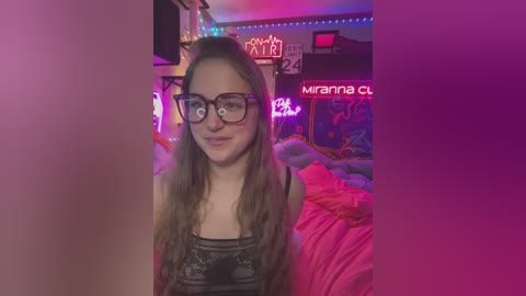 Media: A video of a young, light-skinned woman with long, wavy brown hair, wearing glasses and a black lace top, sitting in a colorful, neon-lit bedroom with a messy bed and wall art.