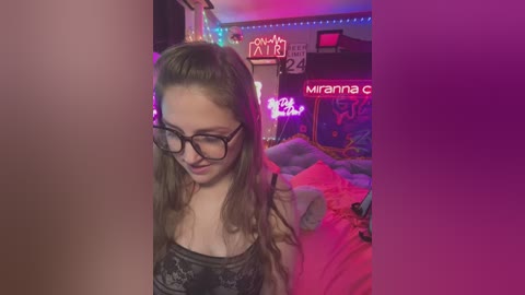 Media: Video of a young woman with light skin and long brown hair, wearing black lace lingerie, glasses, and a playful expression, standing in a colorful, neon-lit bedroom with a large, unmade bed and posters on the walls.